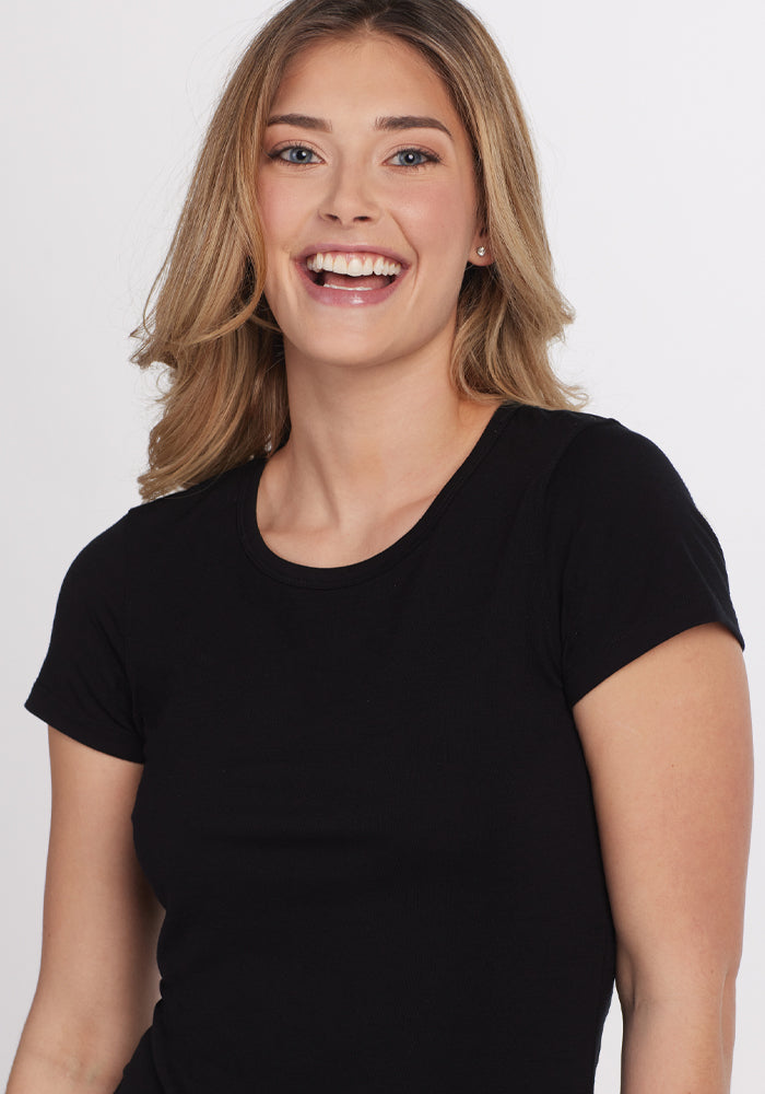 A woman with long hair smiles brightly at the camera, wearing the sleek black Addie Short Sleeve Crew from Woolx, crafted from soft Australian Merino Wool.