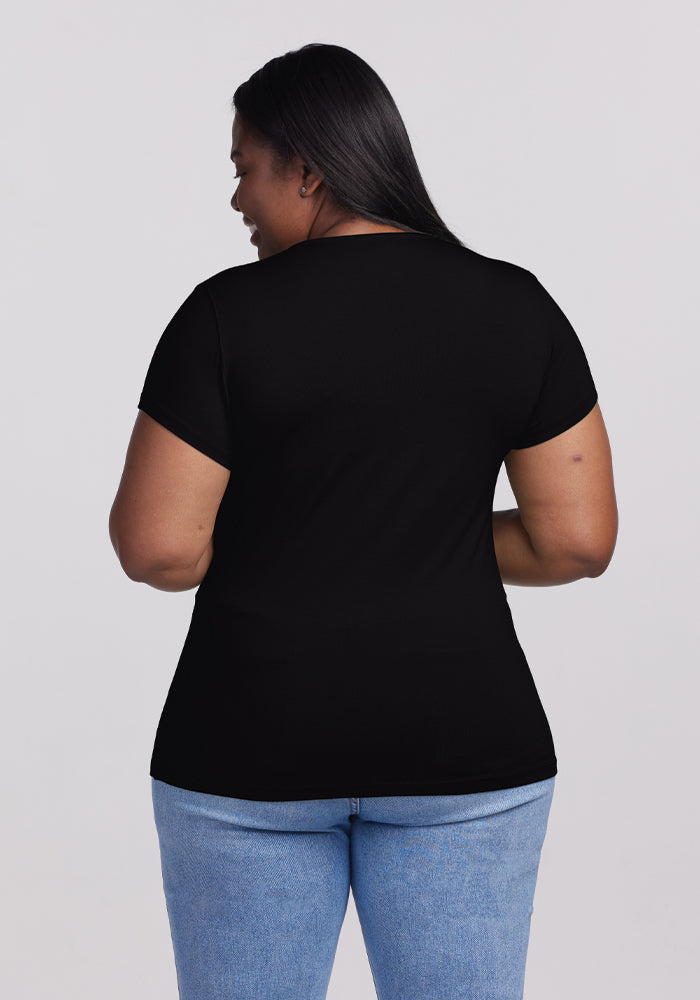 With long dark hair, a person is turned sideways, wearing the Addie Short Sleeve Crew in black by Woolx. This lightweight, odor-free Merino tee pairs with light blue jeans and subtly contrasts against the plain gray background, highlighting their casual style.