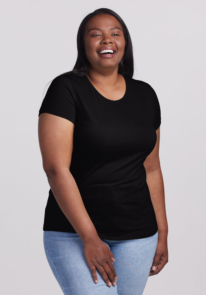 A person wearing the Woolx Addie Short Sleeve Crew in black and light blue jeans stands smiling against a plain light gray background. 