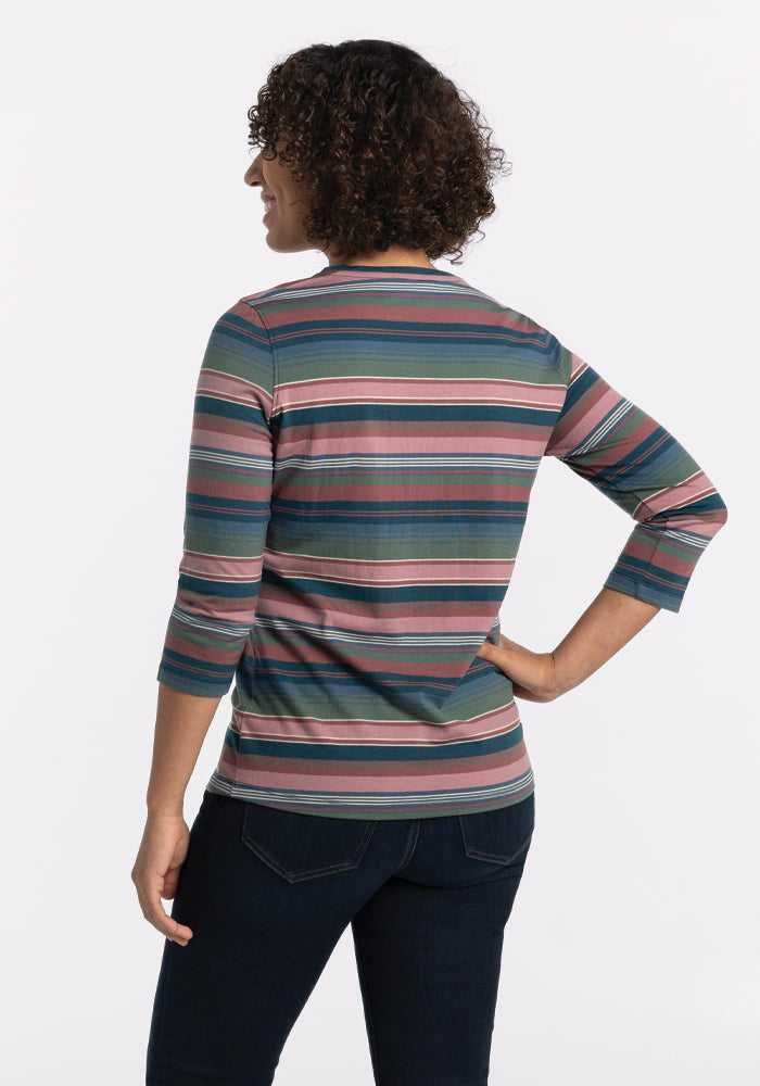 A person with curly hair stands facing away in a Woolx Elena V Neck - Adirondack 2.0 Stripe, expertly crafted from lightweight fabric displaying shades of green, pink, blue, and gray. This stylish top boasts three-quarter sleeves and pairs perfectly with dark jeans against a plain white backdrop.