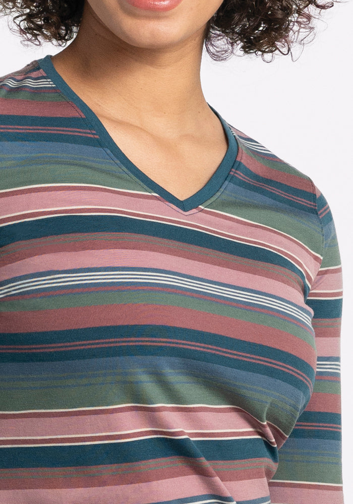 A person is wearing a Woolx Elena V Neck - Adirondack 2.0 Stripe, featuring horizontal stripes in shades of green, blue, brown, and pink. Made from lightweight fabric, the design highlights the upper part of the shirt while partially obscuring the person's face.