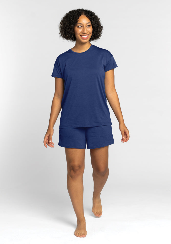 A person with curly hair is seen wearing the Billie Lounge Tee in Starry Night from Woolx, paired with matching shorts made of temperature-regulating fabric, as they walk barefoot against a plain white background.