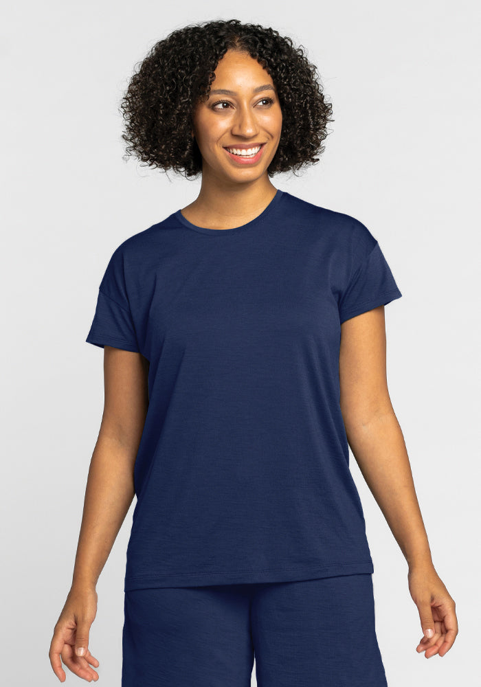 A person with curly hair smiles while wearing the Billie Lounge Tee in Starry Night from Woolx, paired with matching pants against a plain light background.