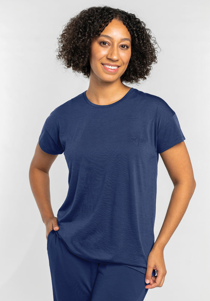 A person with curly hair is smiling and wearing the Billie Lounge Tee in Starry Night by Woolx, paired with matching moisture-wicking pants, standing against a plain background.