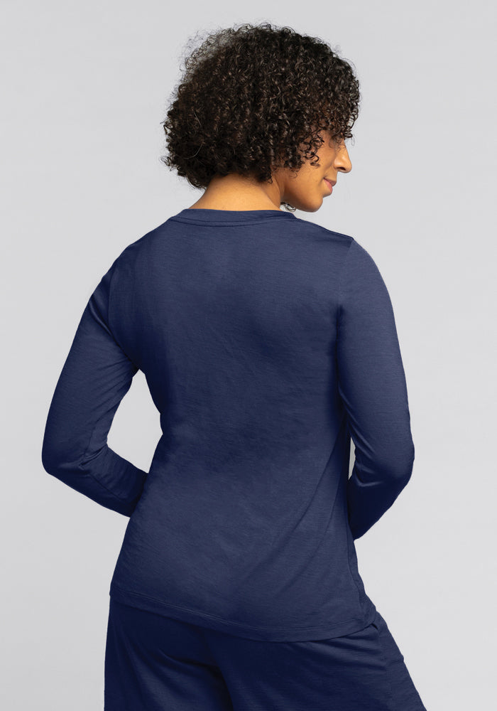 A person with curly hair is seen from the back, wearing a navy blue Lily V Neck Lounge Top by Woolx and matching pants, standing against a plain light gray background.