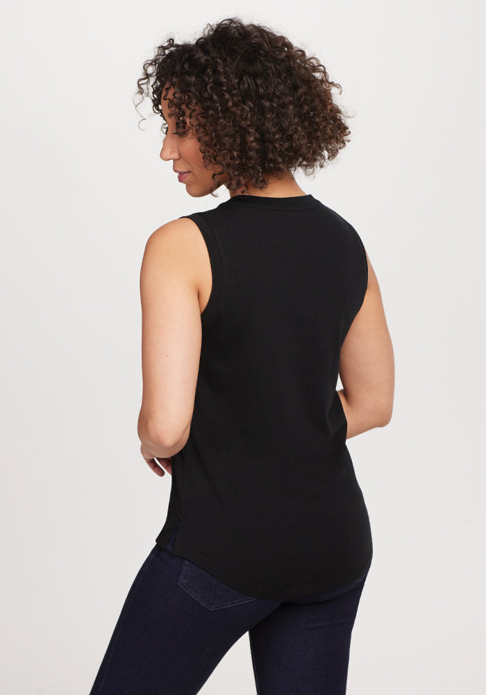 A person with curly hair is wearing a sleek Bella Tunic Top in black from Woolx and dark jeans, facing slightly away from the camera against a plain white background.