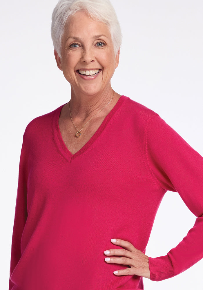 An older woman with a joyful smile and short, white hair stands against a plain white background, wearing the Woolx Francesca Sweater in Berry Burst.