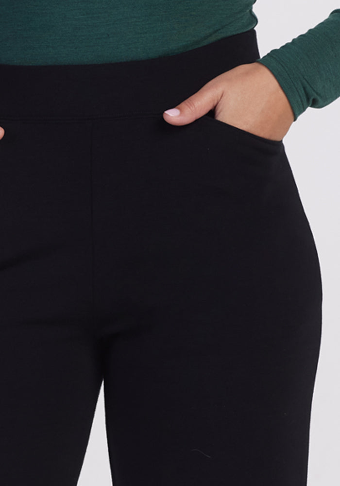 A person with one hand in their pocket is wearing Woolx Ellie Pants and a dark green long-sleeve shirt. The focus is on the waist and upper thighs, showcasing the fit and style of these warm pants.