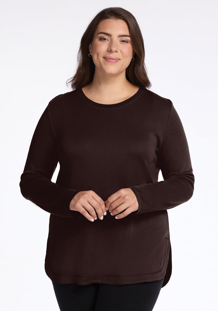 A woman dressed in the Blair Tunic by Woolx, made from odor-resistant merino wool in a French Roast color. 