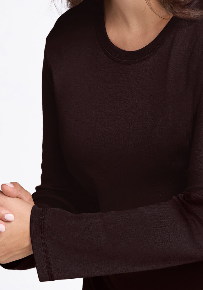 A person wearing a long-sleeved, odor-resistant Blair Tunic in French Roast by Woolx sits with arms crossed. The focus is on their upper torso and arms, set against a white background.