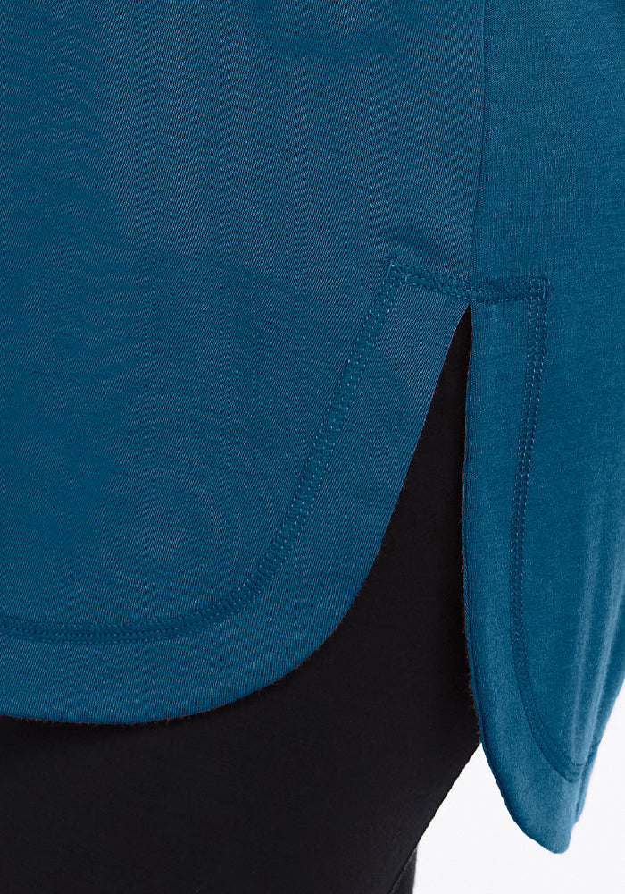 Close-up of the Blair Tunic by Woolx in Real Teal, featuring a rounded hem with a side slit, beautifully displaying teal fabric over black. The visible stitching accentuates its lightweight warmth and elegant design.