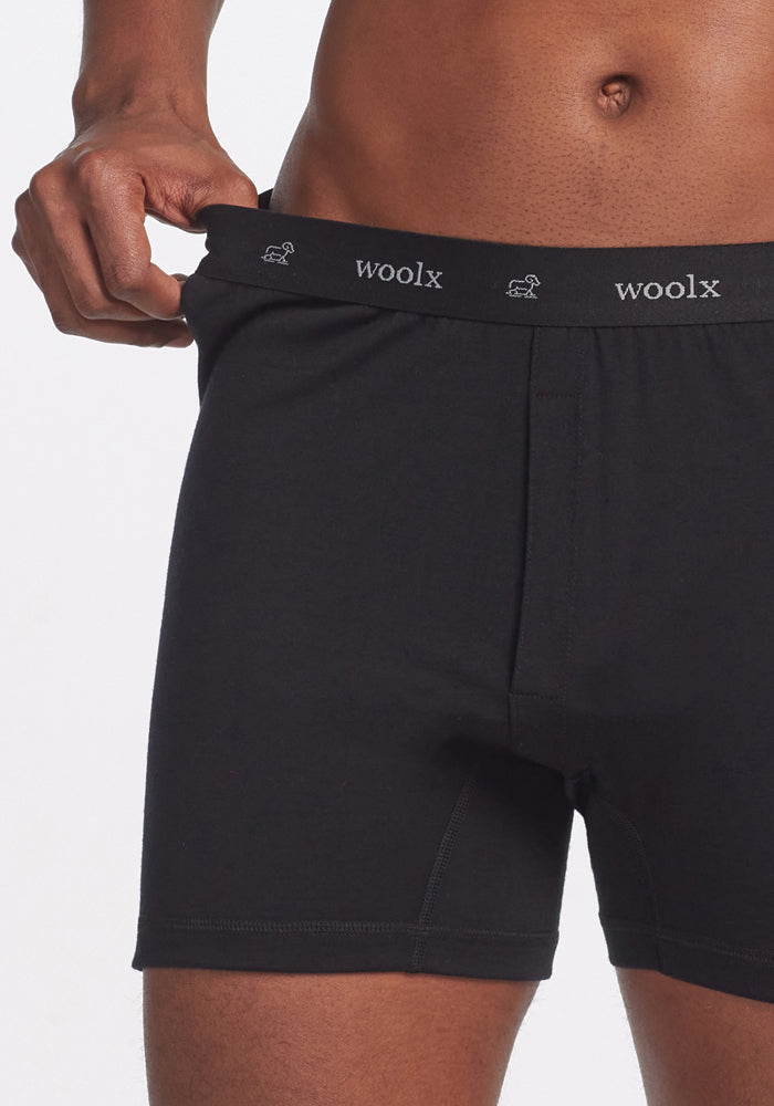 A person is seen wearing the Breathe Boxer Shorts - Black by Woolx, with their hand subtly adjusting the waistband to highlight the fit. Crafted from Australian Merino Wool, these breathable boxer shorts deliver a sleek design along with unmatched comfort and style.