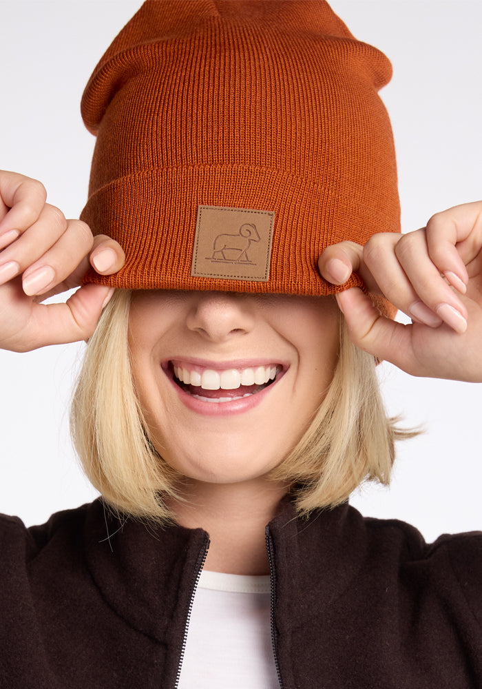 A woman wearing a Woolx Baylor Beanie in the Cinnamon Stick shade, made from merino wool, stands out in the chilly breeze.