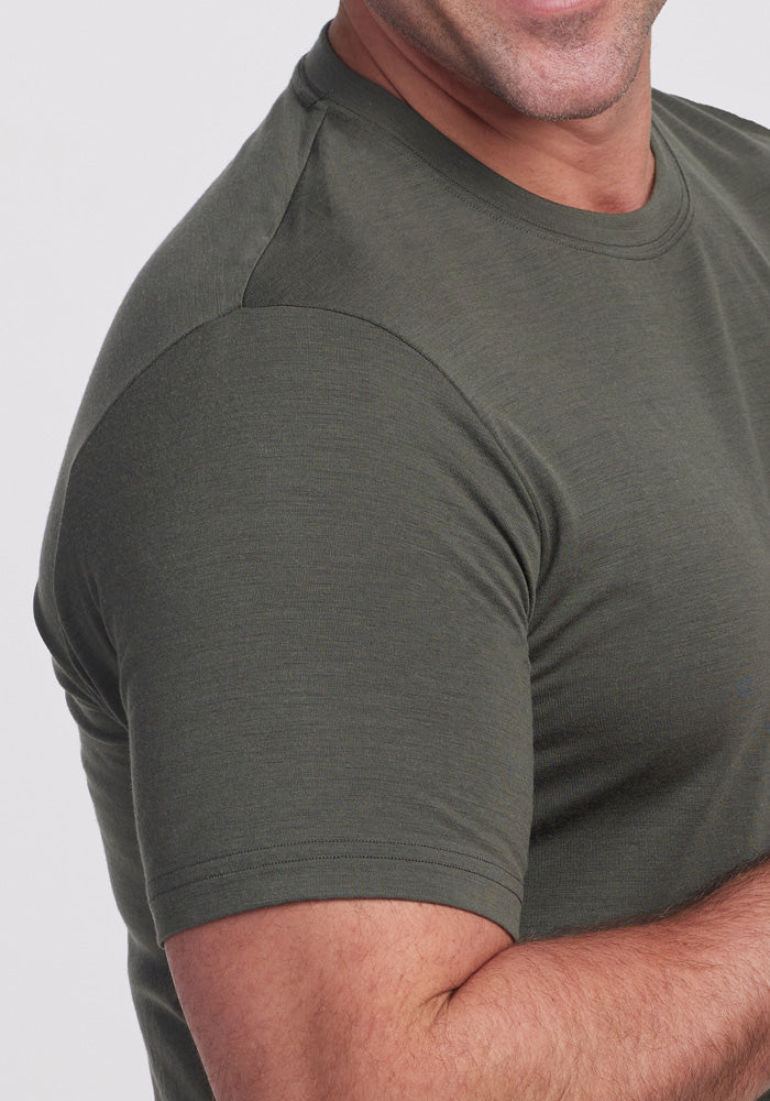 A close-up of a person wearing a fitted, short-sleeve Endurance Tee in Deep Fern by Woolx. The image focuses on their upper body, showcasing the fabric's texture and the sleeve's fit on their arm against a plain white background, exemplifying premium performance gear.