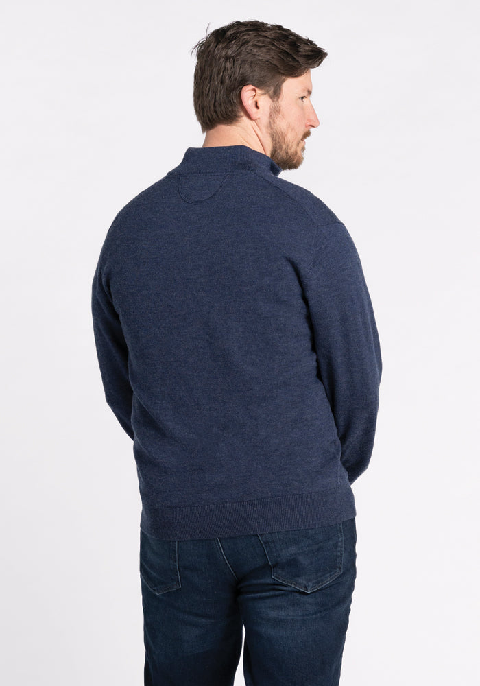 A man with short brown hair is wearing the Woolx Enzo Quarter Zip in Twilight Storm and jeans, standing against a plain white background and facing away from the camera.