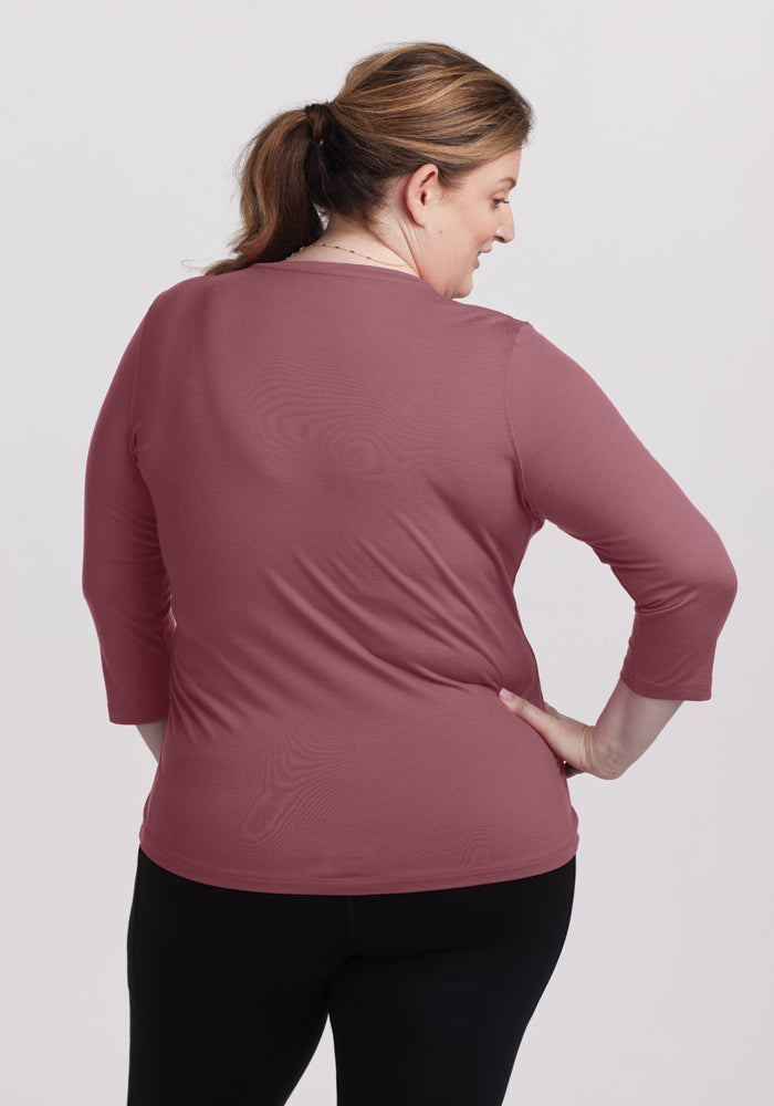 A woman with her hair in a ponytail is shown from the back, wearing a relaxed-fit Elena V Neck Top in wild ginger by Woolx, crafted from merino wool, paired with black pants. The background is plain white.