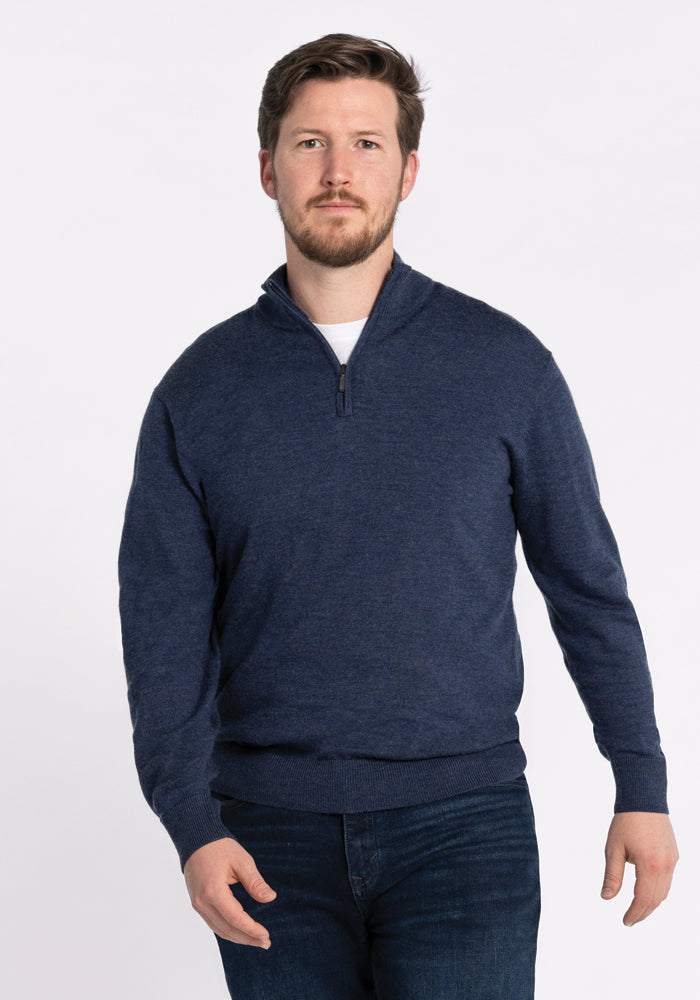 A man with short hair and a beard is wearing the Enzo Quarter Zip in Twilight Storm from Woolx and dark jeans, standing against a plain white background. 