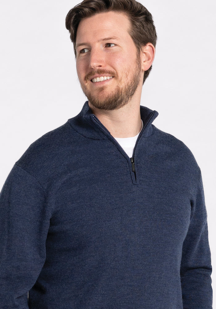 A man with short hair and a beard is smiling and looking off to the side against a plain background while wearing the Woolx Enzo Quarter Zip in Twilight Storm.