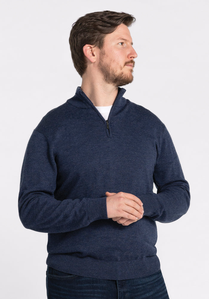 A man with a beard wearing the Woolx Enzo Quarter Zip in Twilight Storm stands against a plain white background, looking to the side with his hands clasped in front of him.