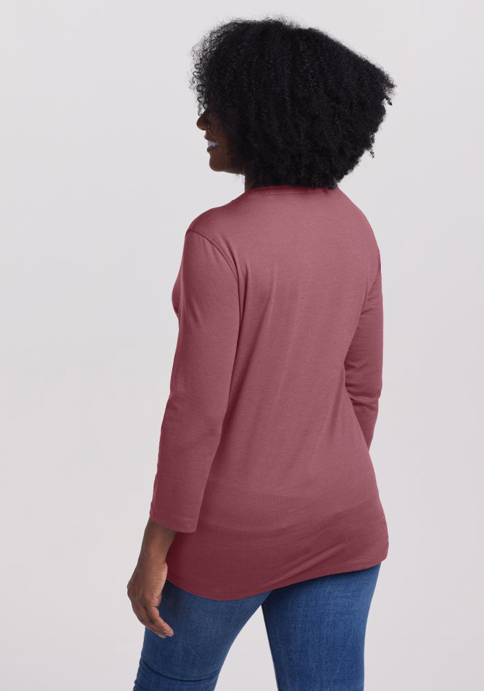 A person with curly hair is wearing a Wild Ginger Elena V-Neck from Woolx, made of Merino wool, paired with blue jeans. The top has a relaxed fit as they stand facing slightly away from the camera against a plain background.