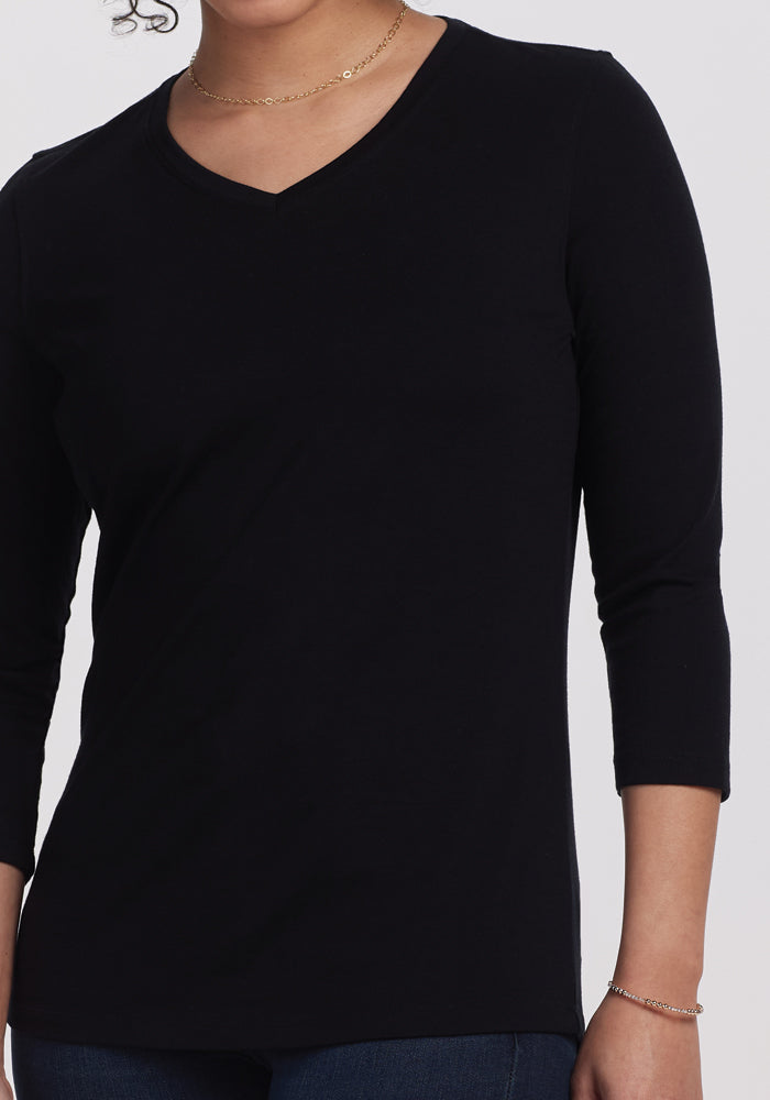 Casual chic is effortlessly embodied with the Elena V Neck from Woolx, a luxurious black merino wool top featuring three-quarter sleeves. Paired with a delicate gold necklace, the ensemble stands out against a minimalist white background.