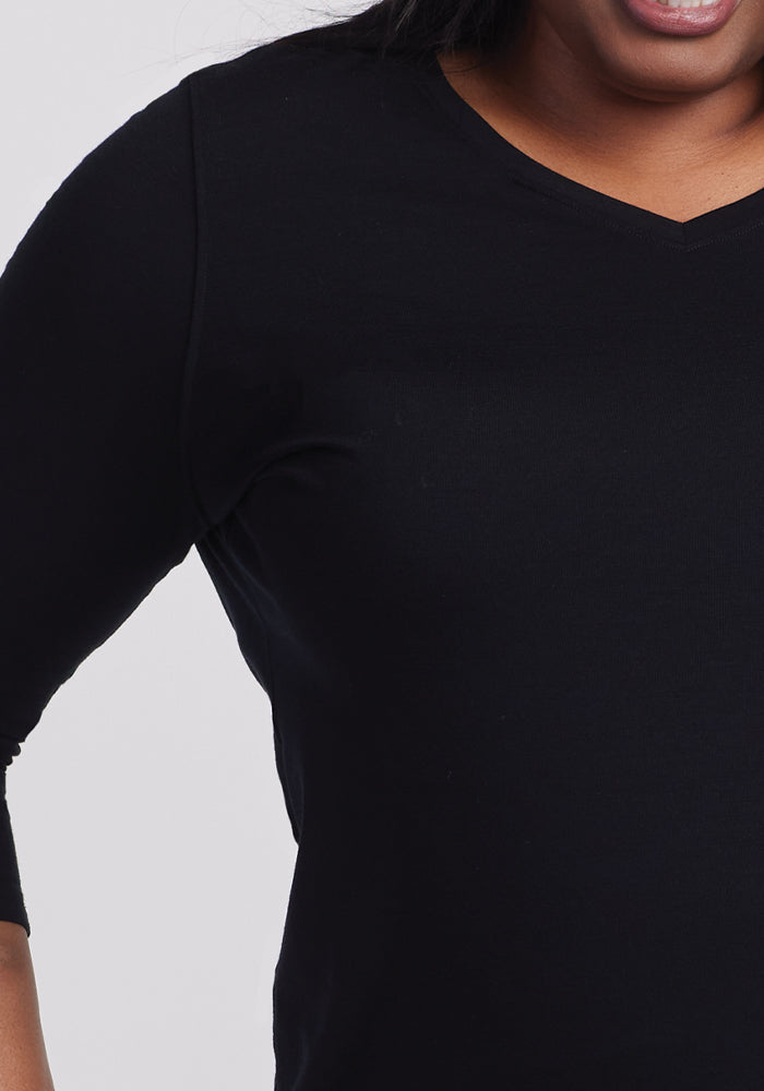 Exuding casual chic elegance, a person effortlessly showcases the Woolx Elena V Neck in black Merino wool. Partially visible from shoulders to midsection, they confidently place their right hand on their hip against a simple white backdrop.