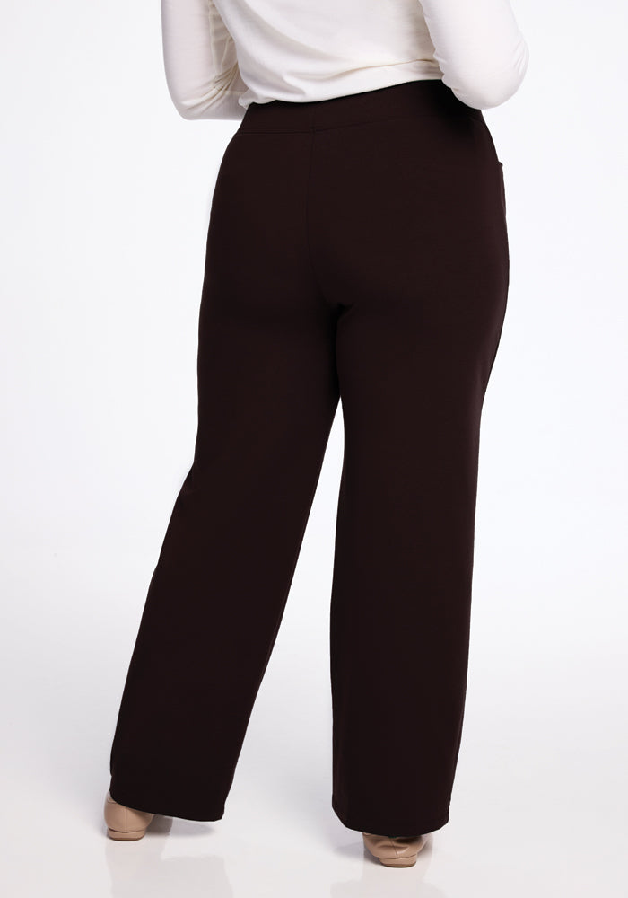 A person is wearing dark brown Ellie Pants by Woolx and a long-sleeved white top, standing with their back to the camera. These warm Ellie Pants contrast beautifully against the plain white background.