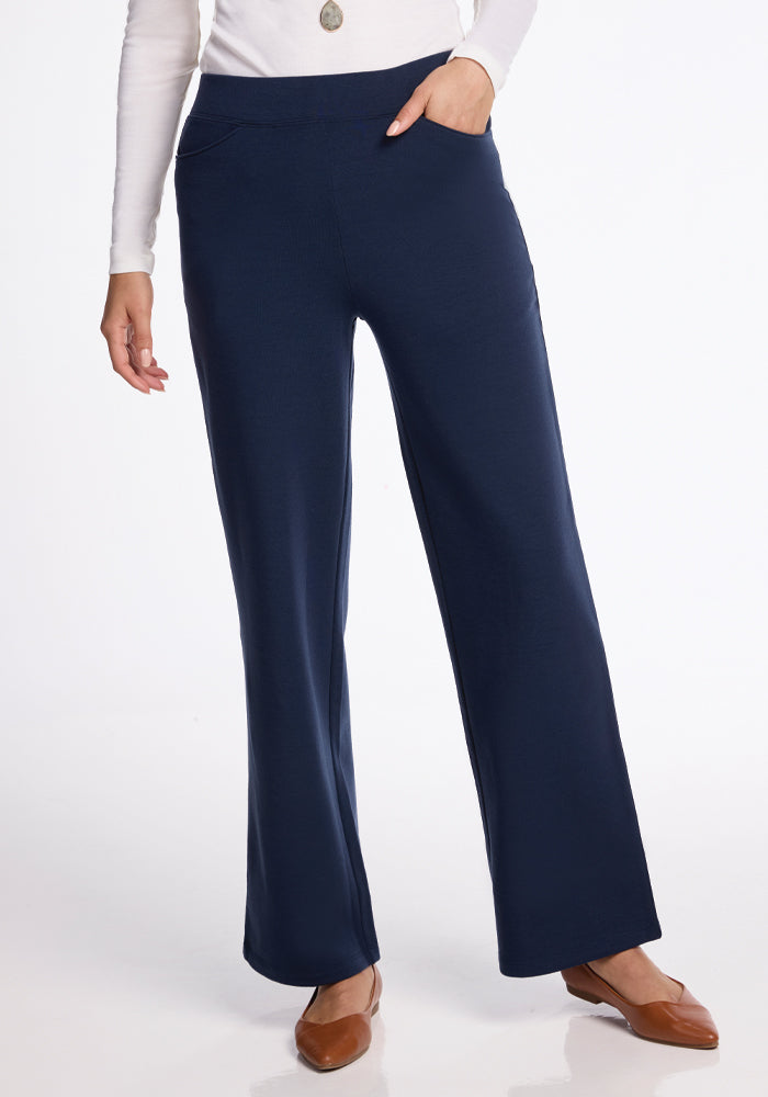 Someone is styled in a white long-sleeve top, paired with the Woolx Ellie Wide Leg Pants in Deep Navy and brown shoes. The striking wide-leg fit stands out against a plain white background, with only the lower half of the body visible. 