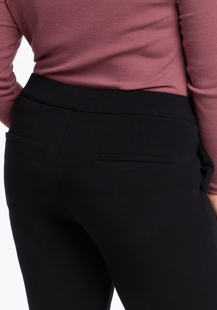 The image features a person wearing a ribbed, long-sleeved pink top and the sleek Emerson Straight Leg Pants Tall in black by Woolx, viewed from the back to highlight the fit of the clothing.