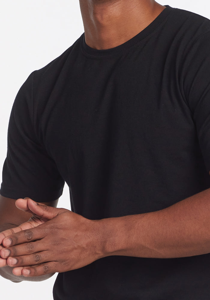 A person wearing a Woolx Endurance Tee - Black clasps their hands together in front of their torso against a plain white background.