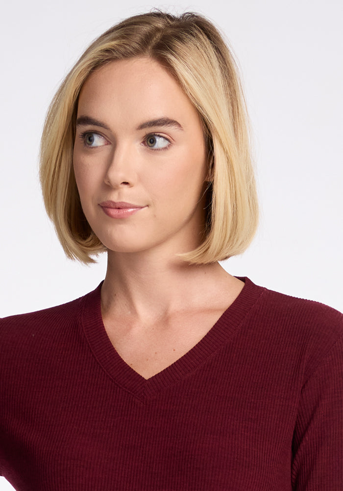 A woman with straight blonde hair cut in a bob is shown from the shoulders up. She is wearing the Woolx Evie Tunic in Cranberry Melange and looking slightly to her left with a neutral expression. The background is plain and white.