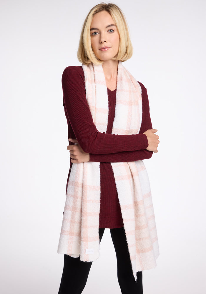 A person with a light blonde bob haircut is wearing the Evie Tunic in Cranberry Melange by Woolx and a white scarf with light pink stripes. They are standing with their arms loosely crossed against a plain white background.