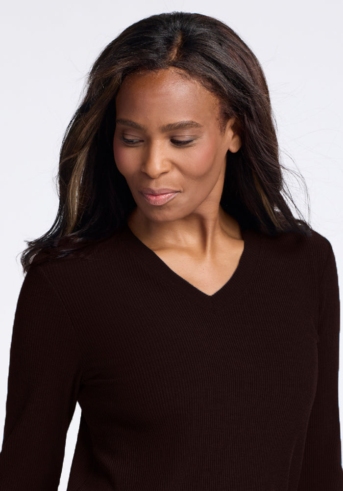 A woman with long, dark hair looks down with a slight smile. She is wearing the Woolx Evie Tunic in French Roast and is set against a plain, light-colored background.