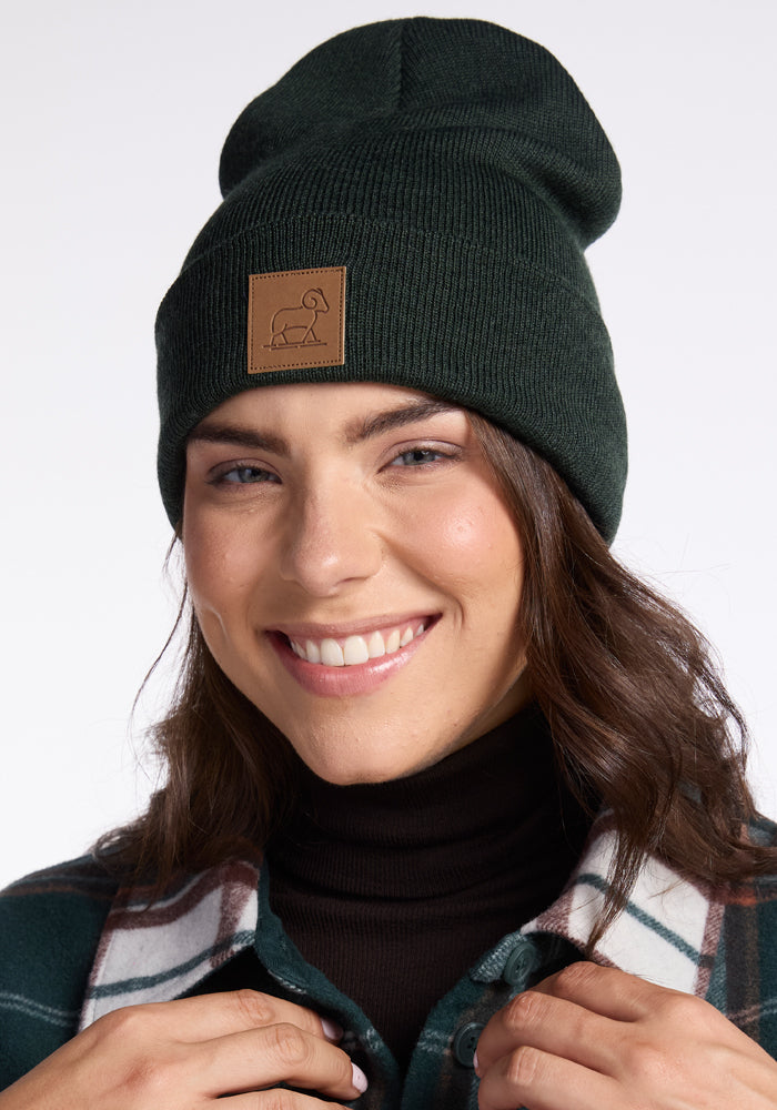 A woman wearing a Baylor Beanie - Pine by Woolx, crafted from cozy Merino Wool, smiles warmly for a picture.