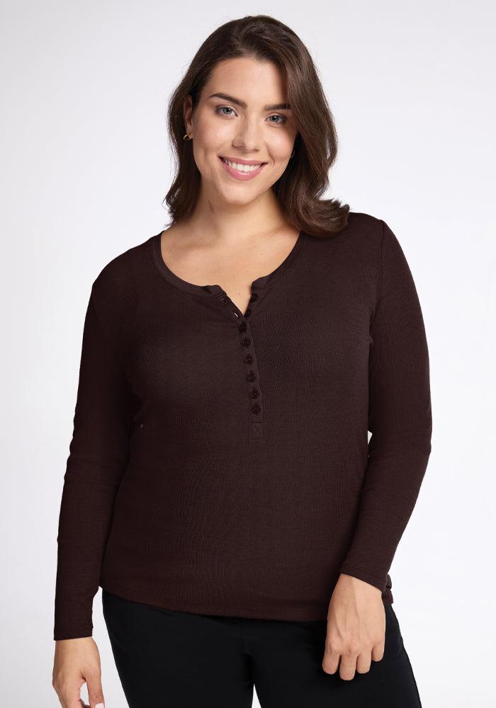 A person with long brown hair is smiling and wearing the Reese Ribbed Henley in French Roast from Woolx, made of soft Merino wool with buttons down the front. The background is plain white. 