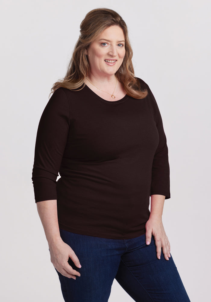 A woman with shoulder-length hair, wearing the Jenny 3/4 Sleeve Crew Neck in French Roast by Woolx and blue jeans, smiles at the camera against a plain white background. 