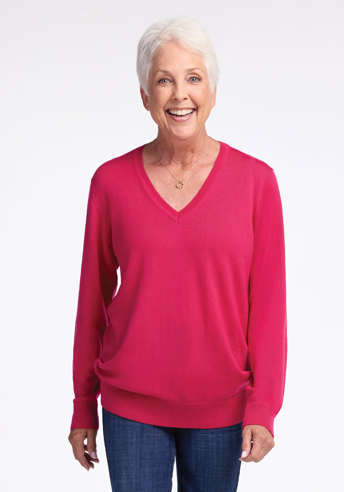 A smiling older woman with short white hair is standing against a plain background. She is wearing the Francesca Sweater - Berry Burst by Woolx and blue jeans. 