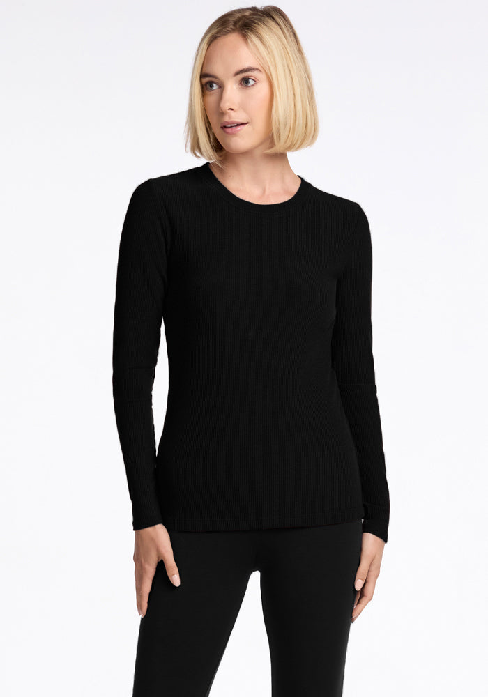 A person with short, blond hair stands against a plain white background, wearing the Hadley Ribbed Crew in black and matching black pants from Woolx. Crafted from luxurious Merino wool, they gaze slightly to the side with a relaxed expression. 