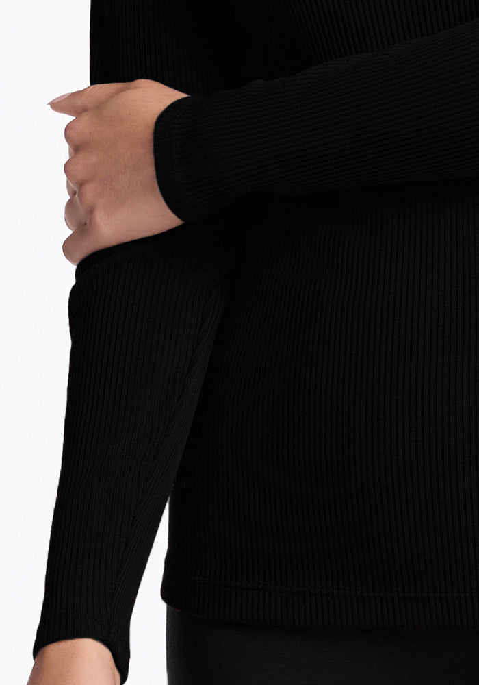 A person is wearing the Hadley Ribbed Crew - Black from Woolx, a luxurious long-sleeve top made of soft Merino wool, with their right arm crossed over their body and gently holding their left sleeve. The white background accentuates the elegance and quality of the fabric.