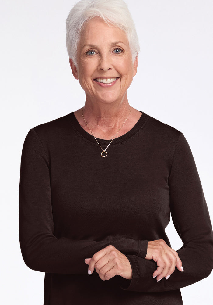 A smiling elderly woman with short white hair, wearing the Woolx Blair Tunic in French Roast and a necklace with a circular pendant, poses confidently against a plain white background.