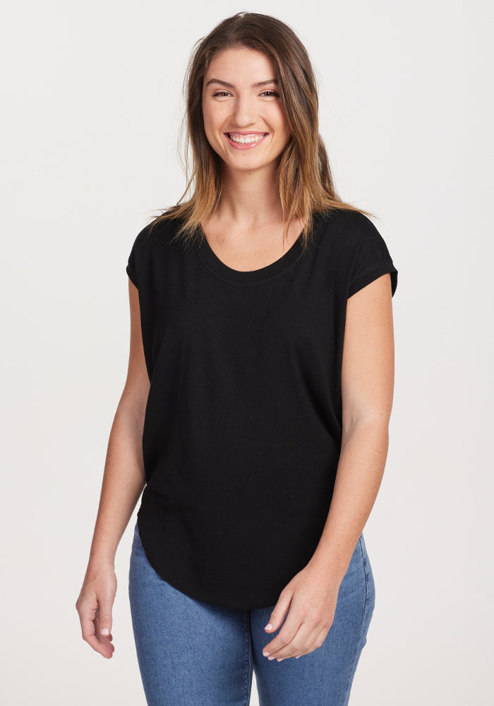 Wearing the versatile Gabi Tunic Top in black by Woolx, a person with long hair smiles while paired with blue jeans, standing against a plain white background. 