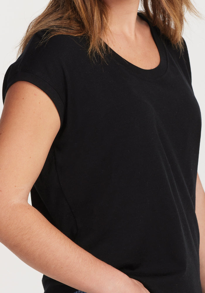 A person wearing the Gabi Tunic Top in black from Woolx stands with their left hand in the pocket. The focus on the upper body, paired with a neutral background, highlights the casual and adaptable style of this top.