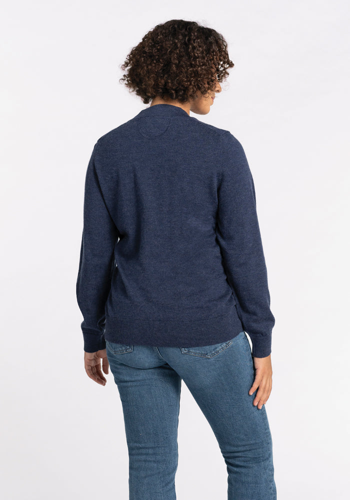 A person with curly hair is wearing the Woolx Gia Sweater in Twilight Storm and blue jeans, standing with their back to the camera against a plain white background.