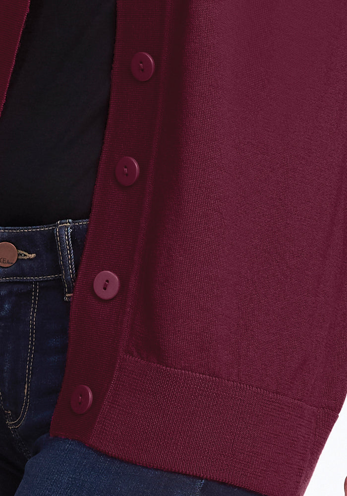 Close-up of a person wearing the luxurious Gia Sweater - Cabernet Crush by Woolx, featuring dark buttons over a black top. The lower portion of the sweater is shown alongside part of blue denim jeans, creating a stylish yet casual outfit.