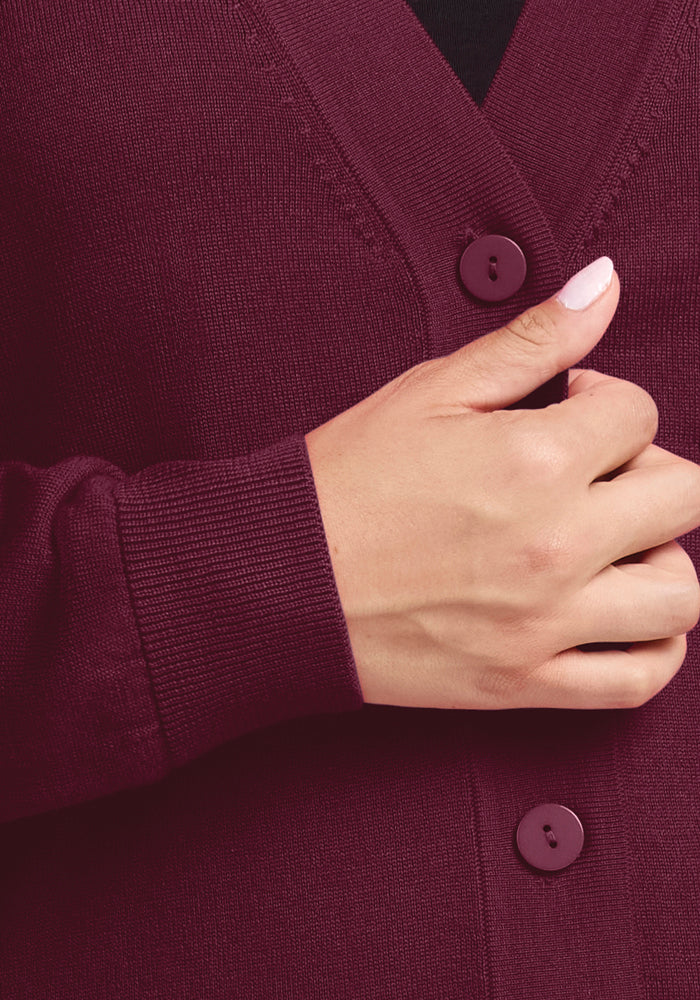 A person wearing a Gia Sweater in the captivating shade of Cabernet Crush is adjusting the garment. Their hand, with neatly manicured nails, emphasizes the luxurious texture of Woolx's Merino wool. The focus is on the rich color and fine details of this exquisite piece of luxury knitwear.