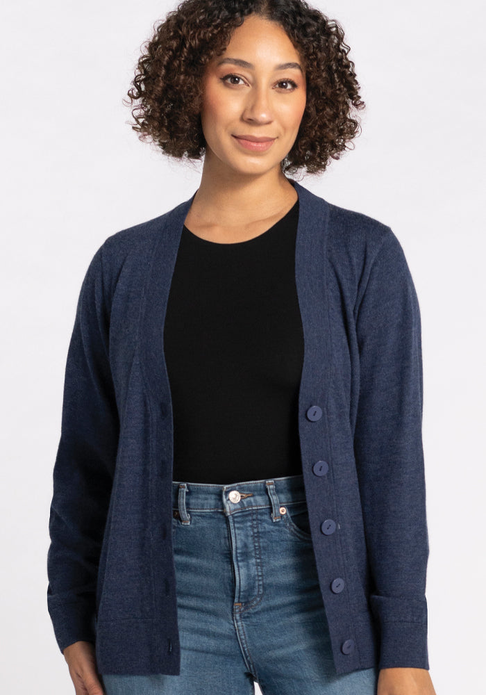 A person with curly hair is wearing the Gia Sweater in Twilight Storm by Woolx over a black top and jeans, standing against a plain background.