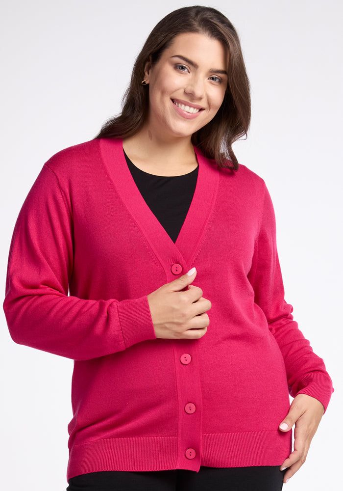 A person wearing the Woolx Gia Sweater in Berry Burst over a black top smiles at the camera. Their long brown hair cascades down, and they stand against a plain white background, exuding lightweight warmth in their stylish merino wool ensemble.