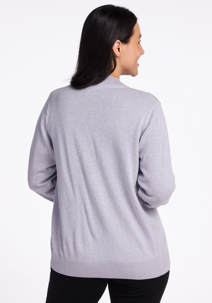 A person with long dark hair is wearing the Woolx Gia Sweater in Mist, positioned against a plain white background. This travel-ready sweater exudes an effortlessly stylish appearance, making it ideal for any journey.