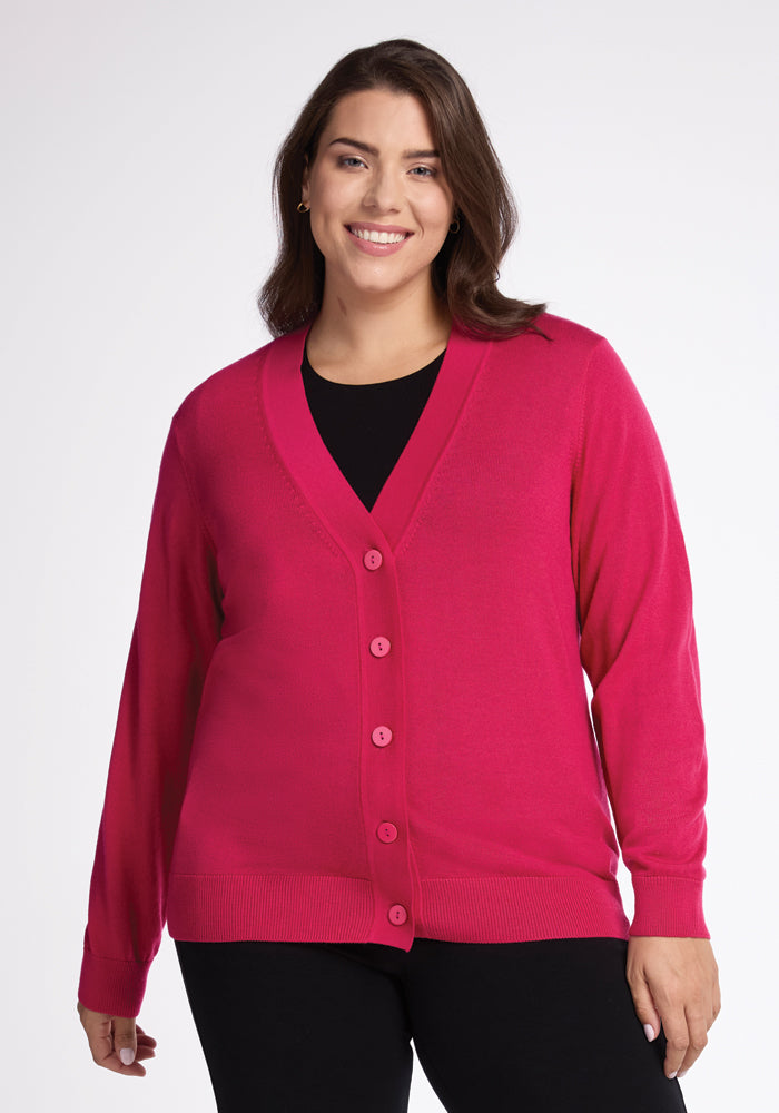 A woman with long, dark hair smiles while wearing the Gia Sweater - Berry Burst by Woolx over a black top. She stands against a plain white background. 