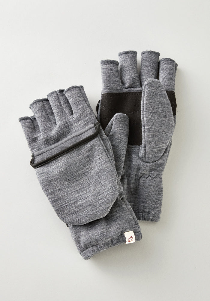 A pair of Cameron Glove Mitten in Graphite Heather by Woolx, featuring black detailing and crafted from a merino wool blend with a foldable mitten flap, rests on a light surface.